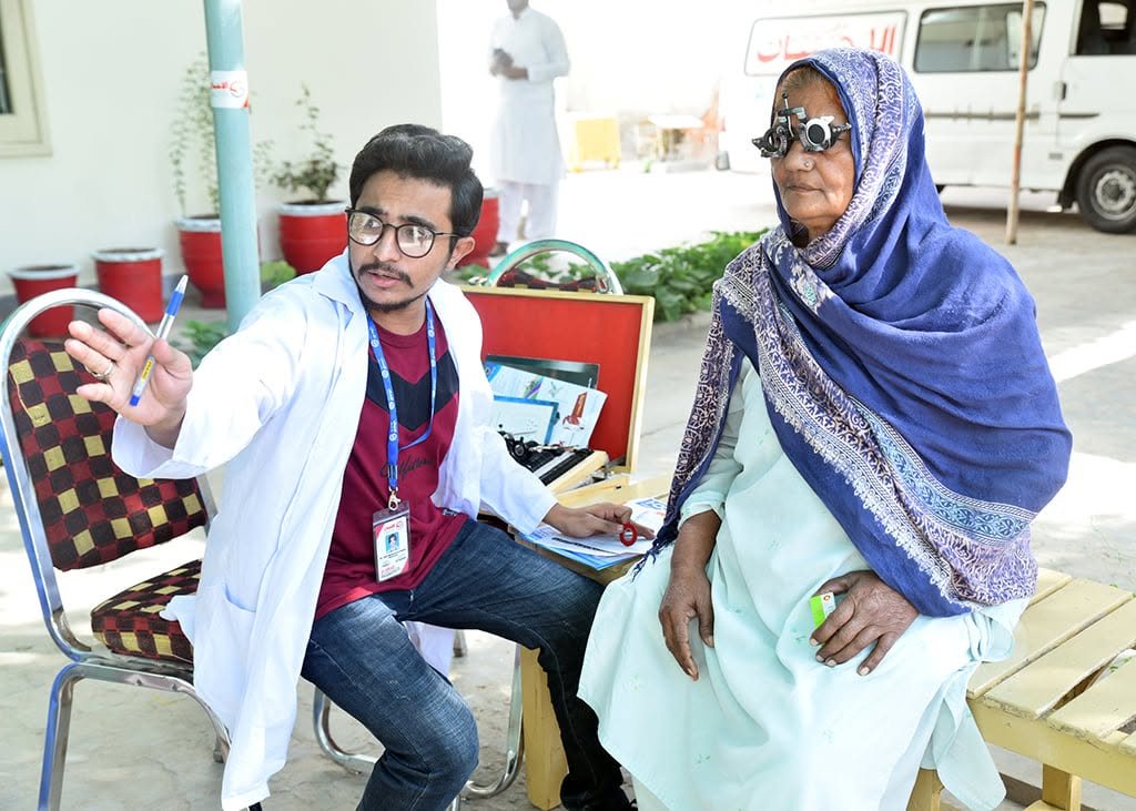 An optometrist testing an elderly woman’s eyesight with a trial frame at a Salma Khatoon Foundation free eye camp in Sahiwal