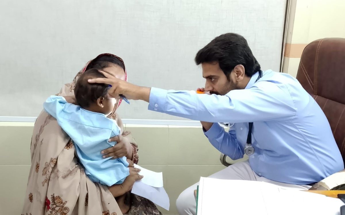 A doctor at the Salma Khatoon Health Center examining a young child held by his mother